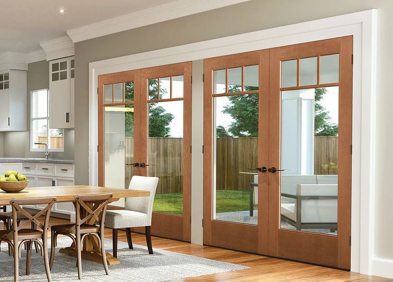 Angled wide shot of two sets of craftsman style double full-lite pecan wood doors leading from a dining room with hardwood floors to an outdoor patio.