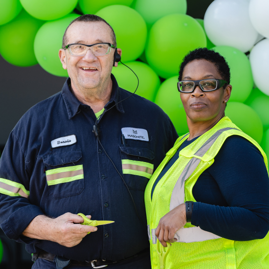 Two Masonite employees, one man and one woman, standing in front of a balloon arch of green and white balloons